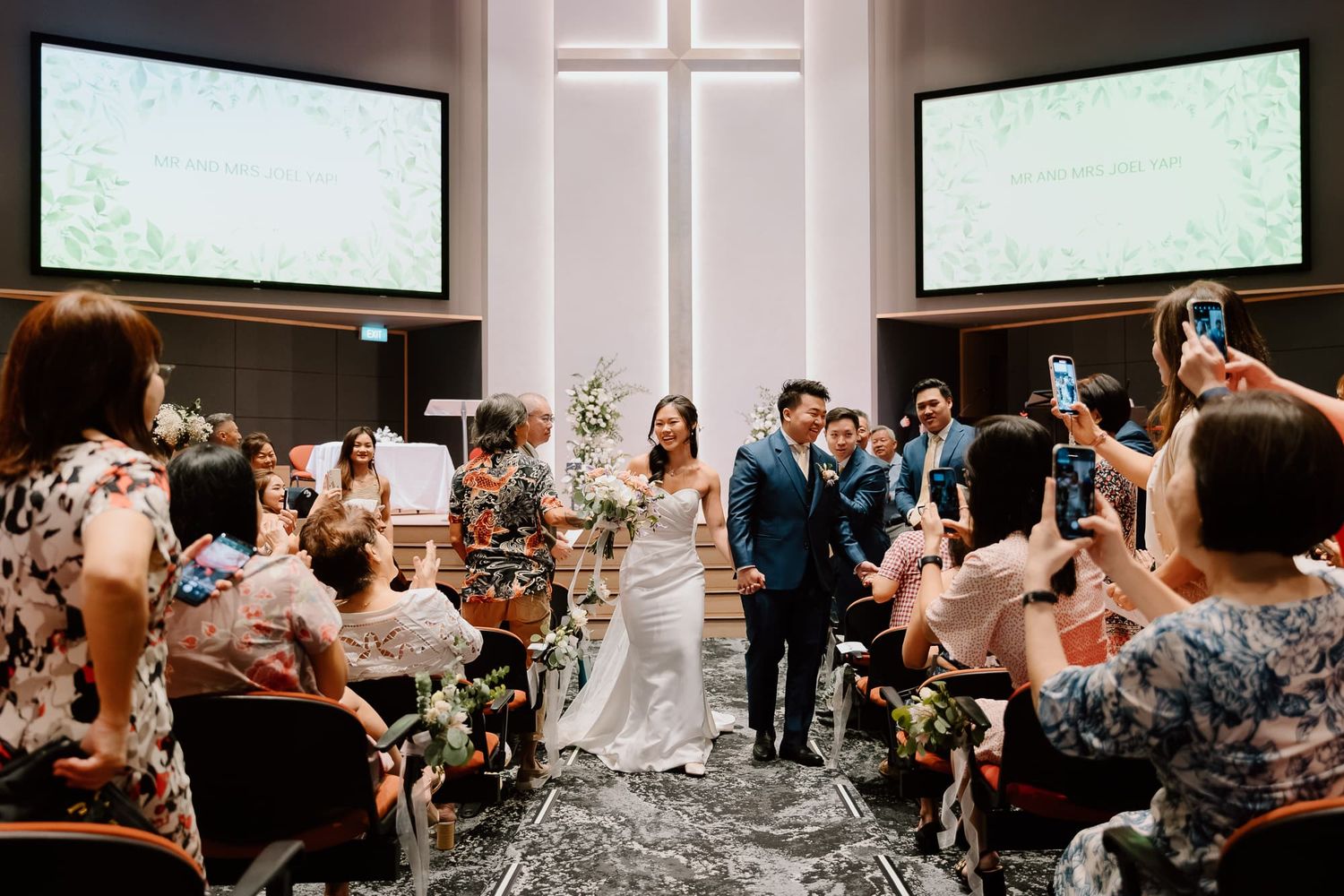 Wedding guests sit in rows of chairs watching a performance in an indoor venue.