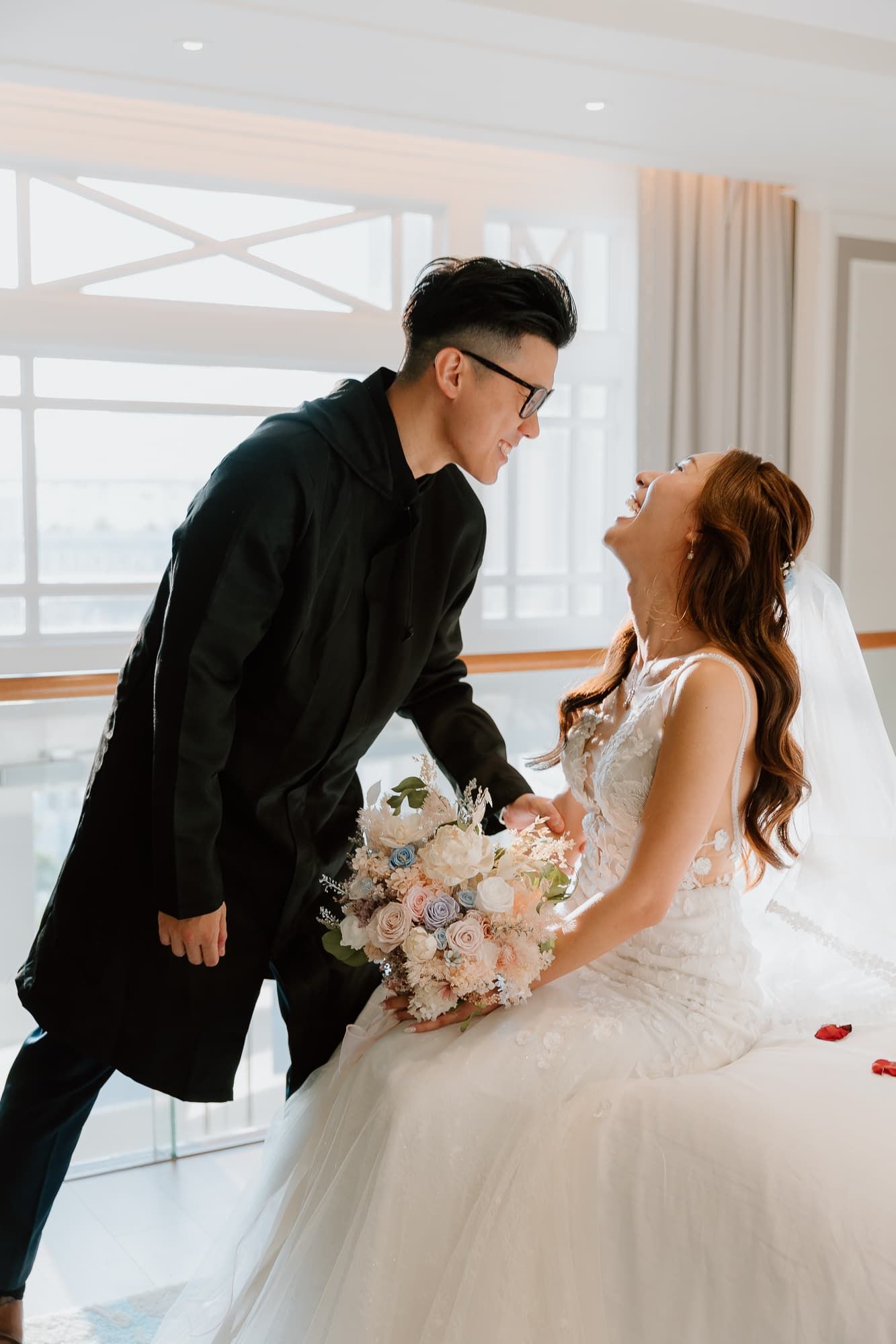 Joyful wedding couple shares intimate moment while holding pink and white bouquet.