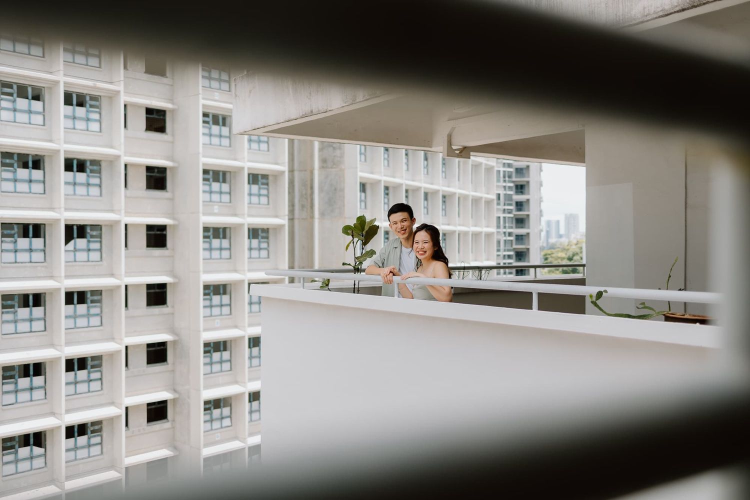 Couple standing on a modern high-rise apartment balcony overlooking city buildings.