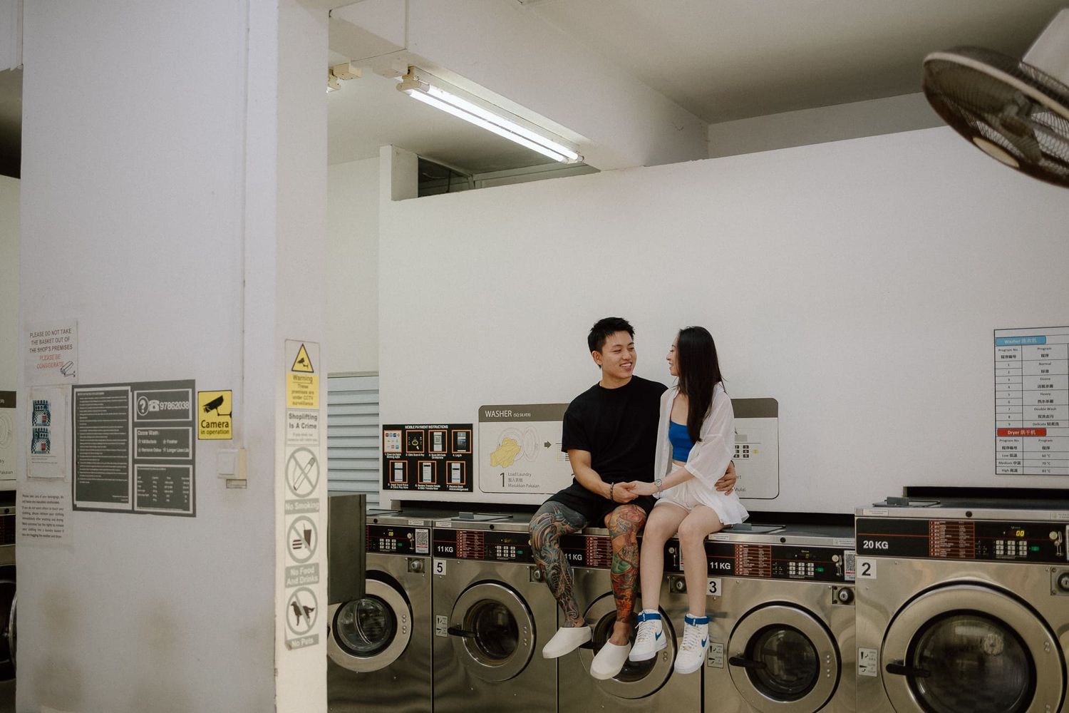 People sitting in a laundromat with washing machines and dryers visible in the background.
