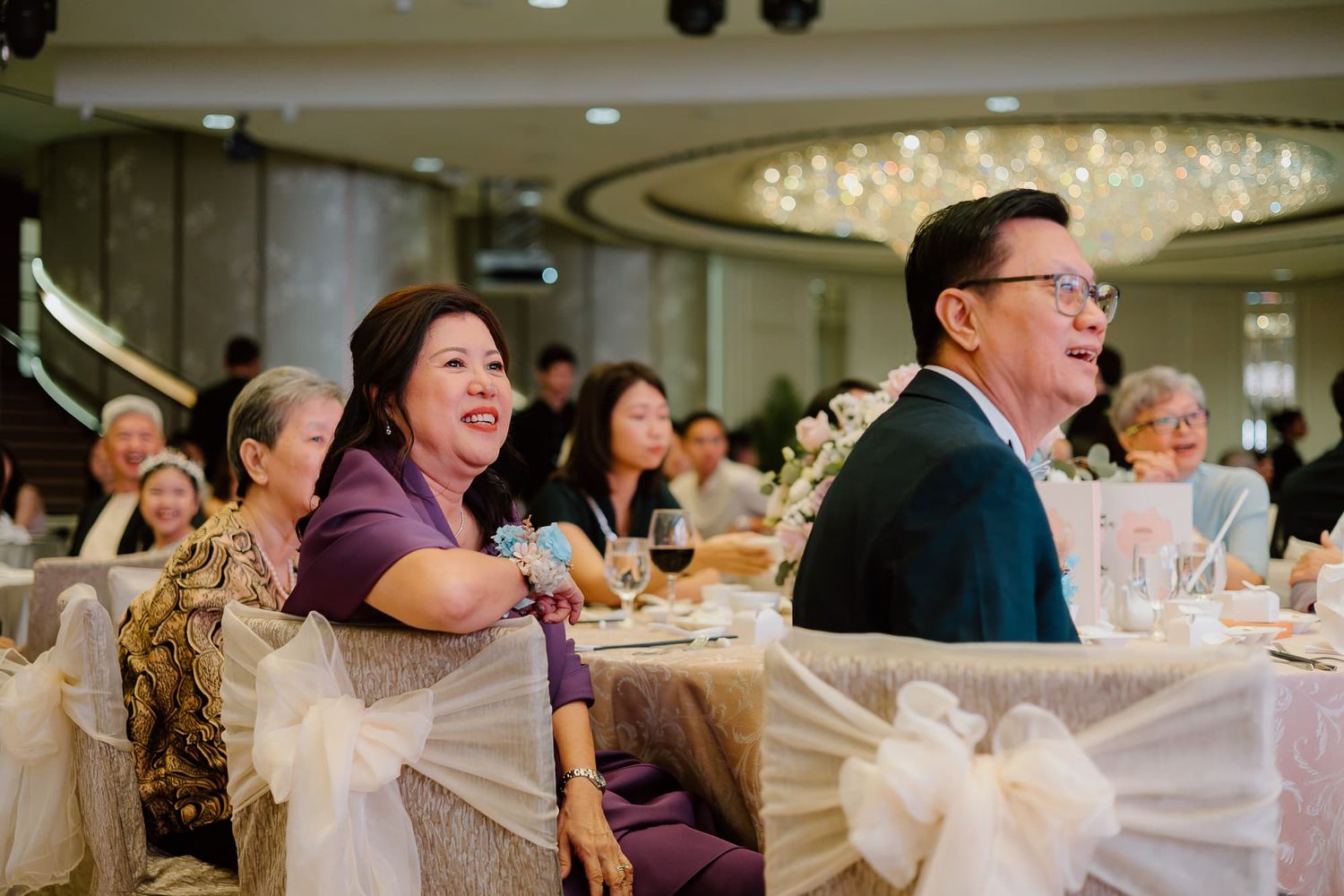 Wedding guests enjoying a celebration dinner in an elegant ballroom with crystal chandeliers.