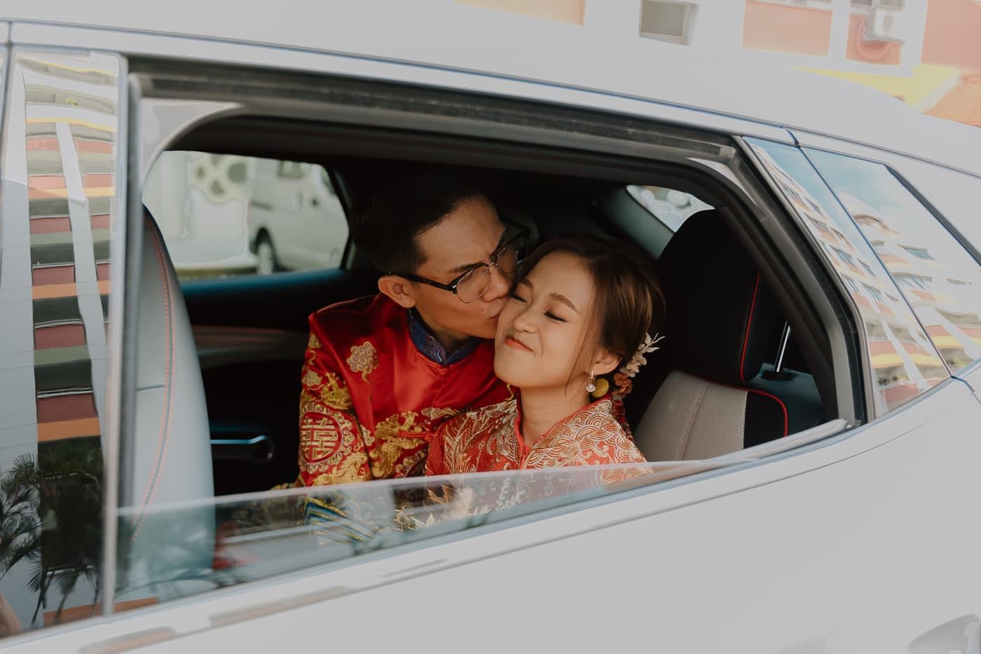 Couple in red traditional wedding outfits sharing an intimate moment in a car.