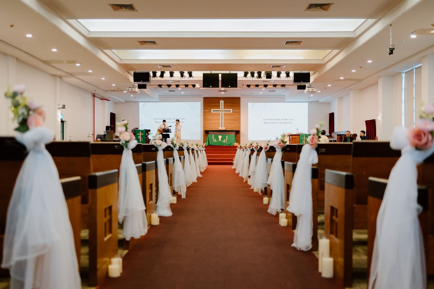 An empty church aisle decorated with white tulle bows and floral arrangements.