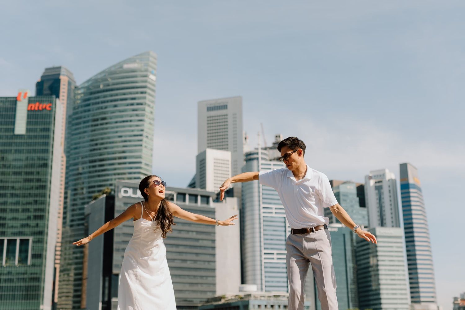 A couple strikes playful poses against a backdrop of modern skyscrapers.