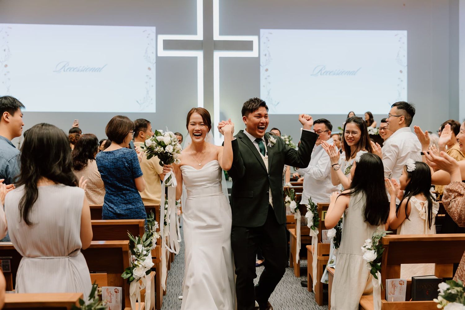 Wedding celebration with guests applauding in modern church venue with cross backdrop.