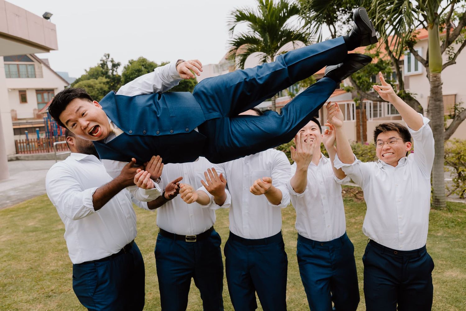 Groomsmen perform fun jumping poses outdoors in navy suits.