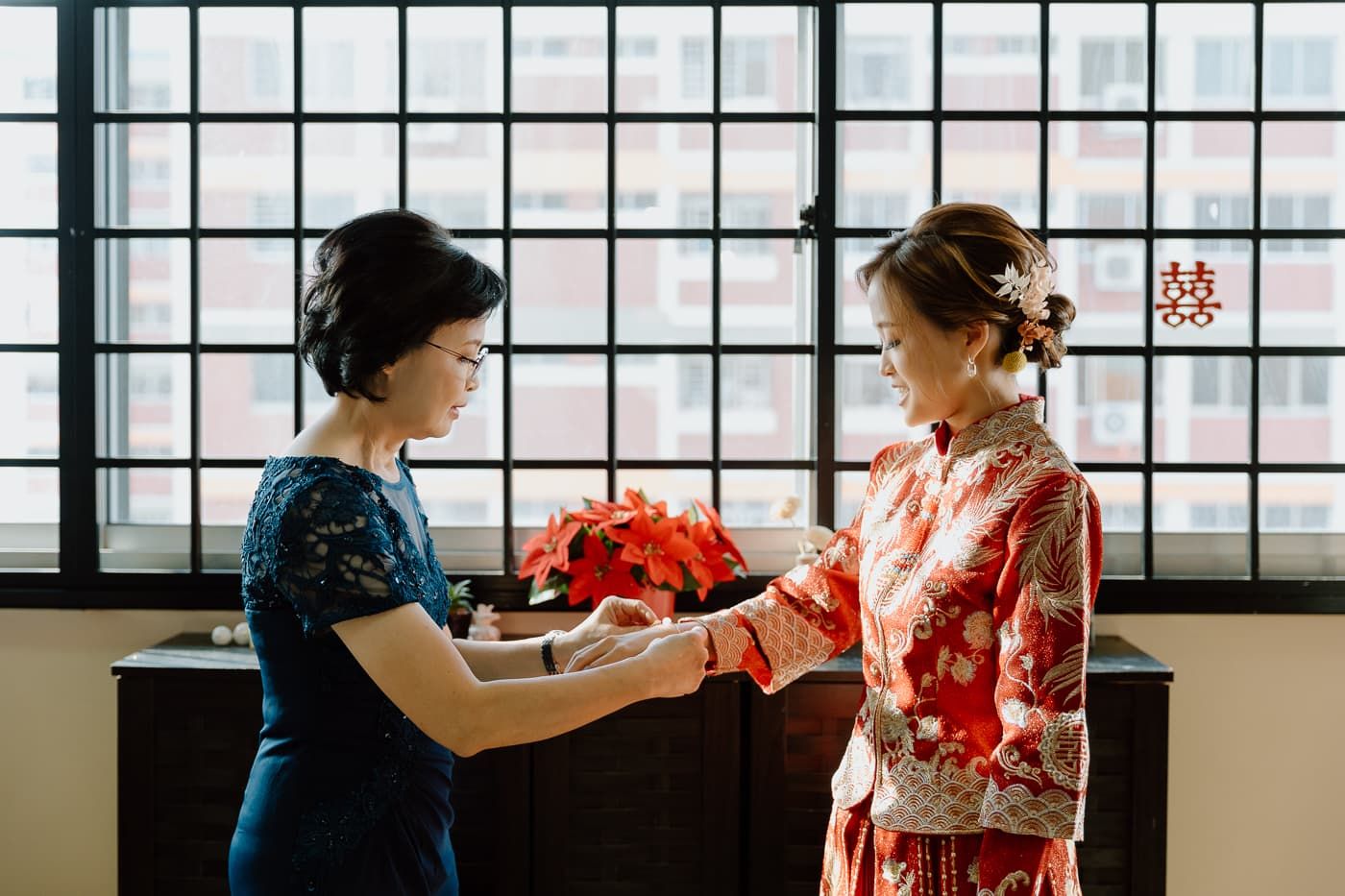 Two people in traditional dress exchanging gifts in front of a window.