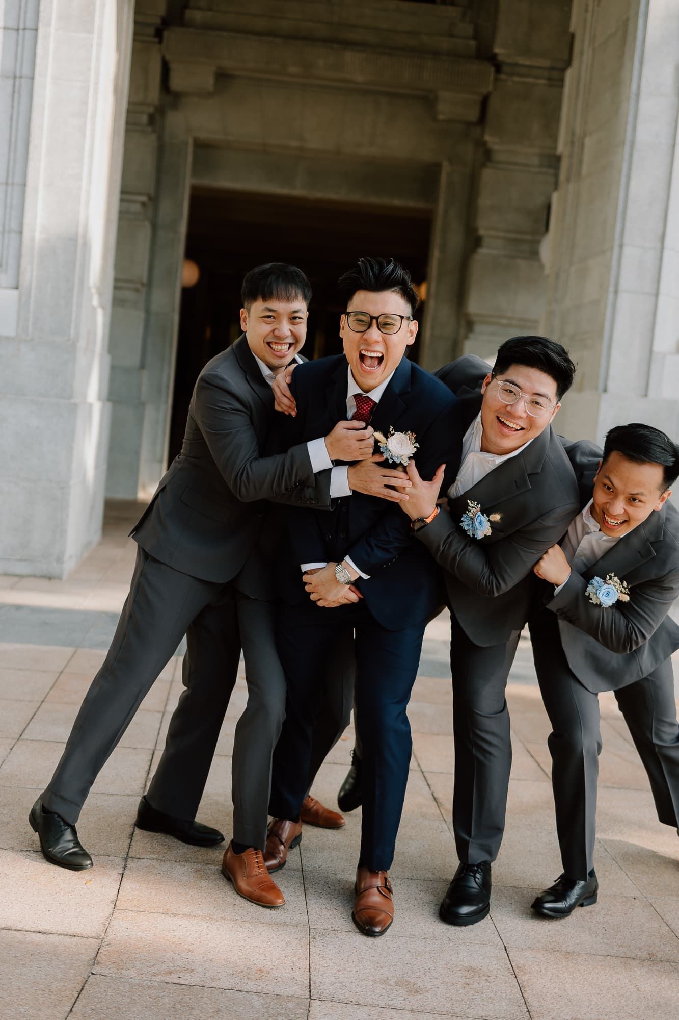 Groomsmen in formal attire sharing a lighthearted moment under an architectural archway.