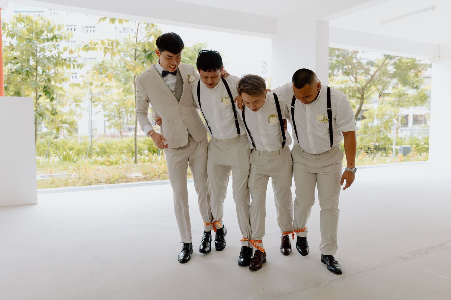 Wedding party members in white suits pose together in a bright corridor.