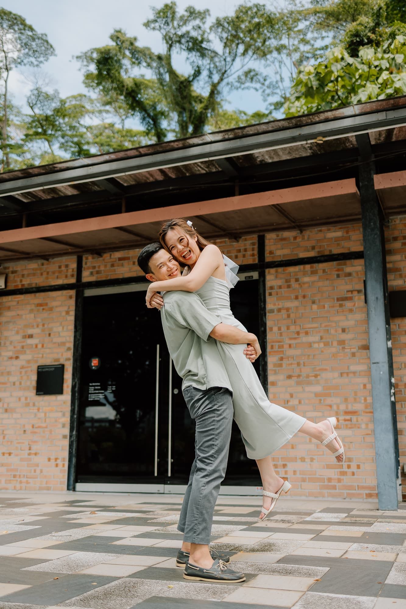Joyful couple embracing in playful lift pose outside brick building.