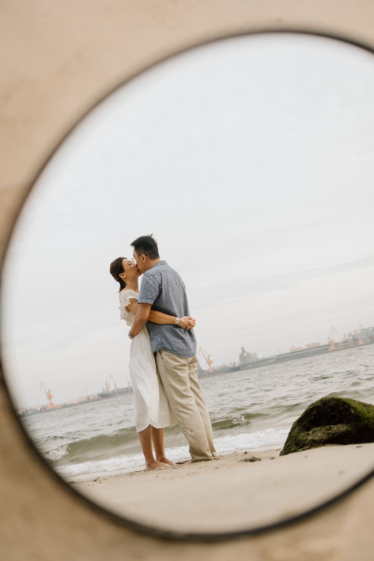 A couple sharing an intimate moment on the beach photographed through a circular frame.