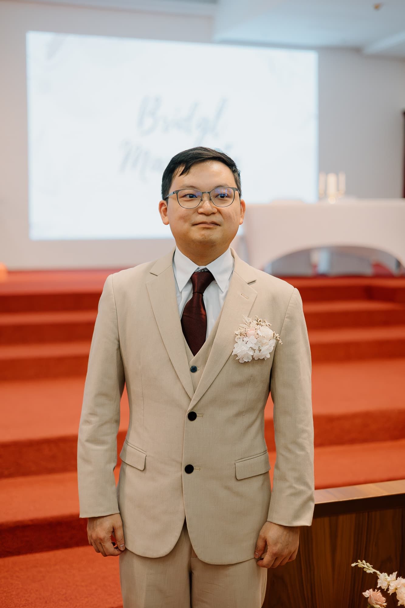 Formal event photo showing beige suit attire against red carpeted backdrop.