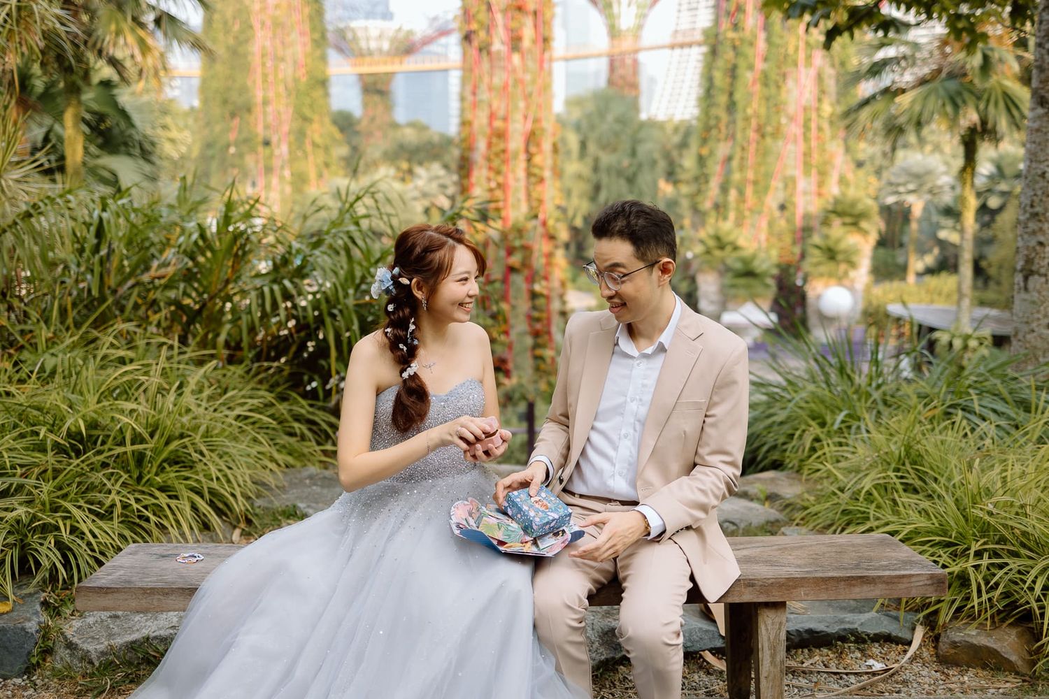 A couple in wedding attire sharing a moment on a bench surrounded by lush greenery.
