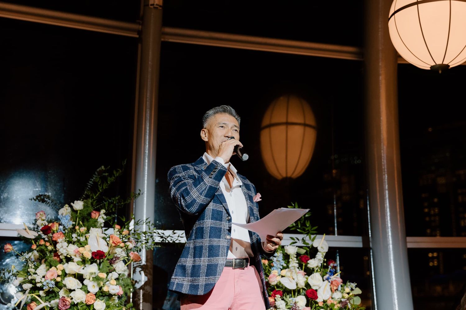 Wedding speaker delivers speech at podium with floral arrangements.