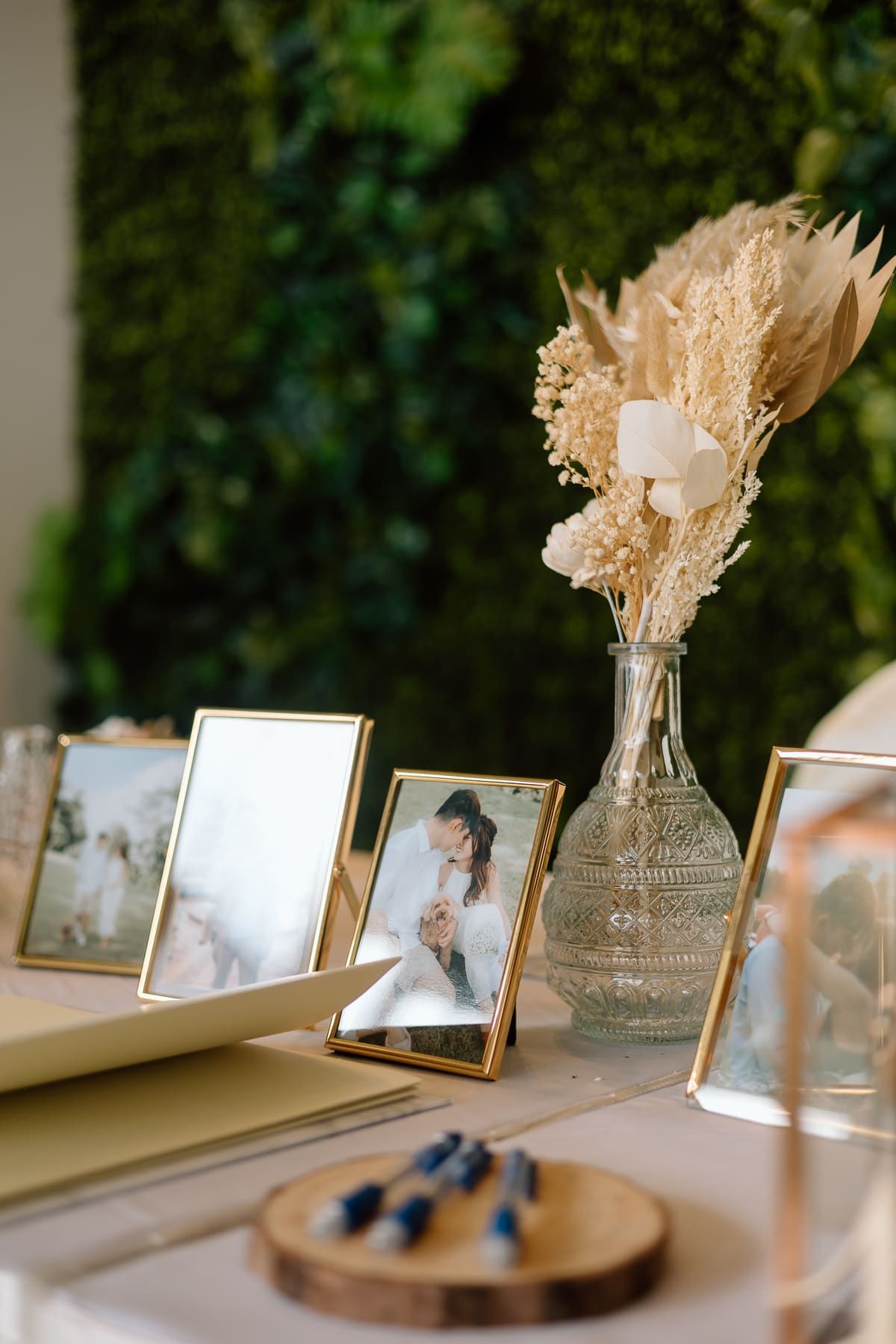 Wedding photo display on wooden tables with dried floral arrangements in vases and framed pictures.