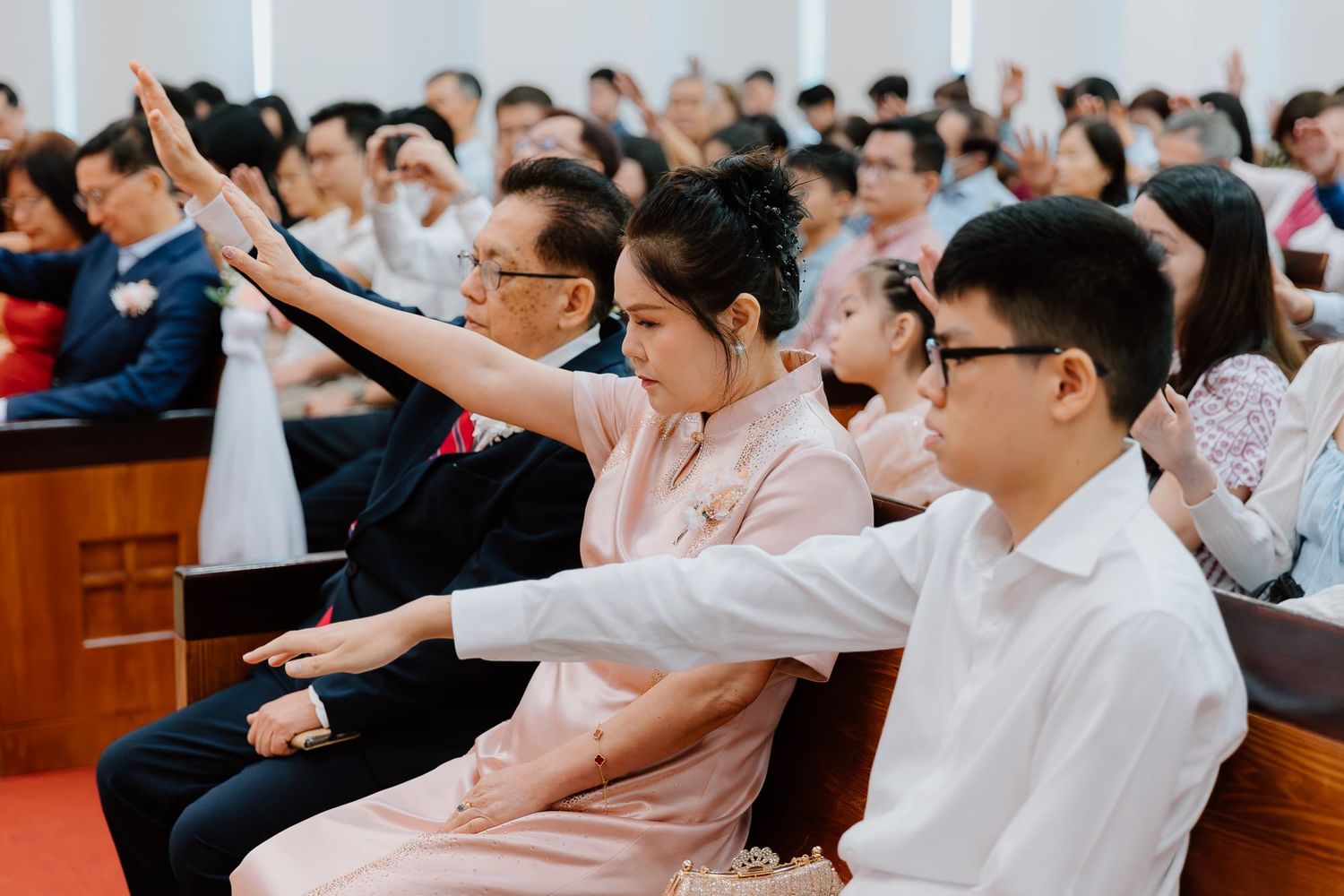 Wedding congregation raises hands during worship service in church sanctuary.