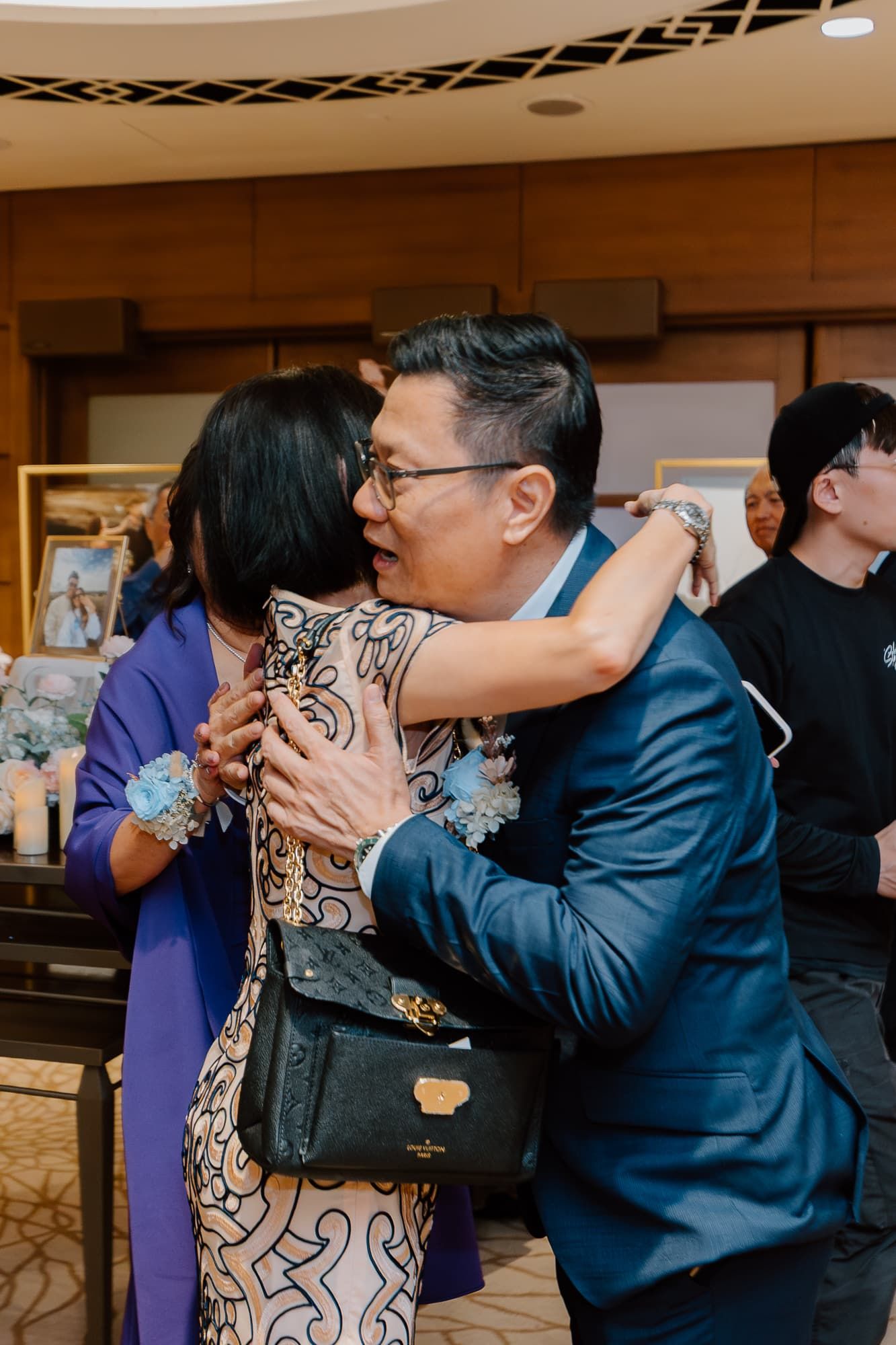 Wedding guests embrace during reception celebration in elegant venue with patterned carpet.