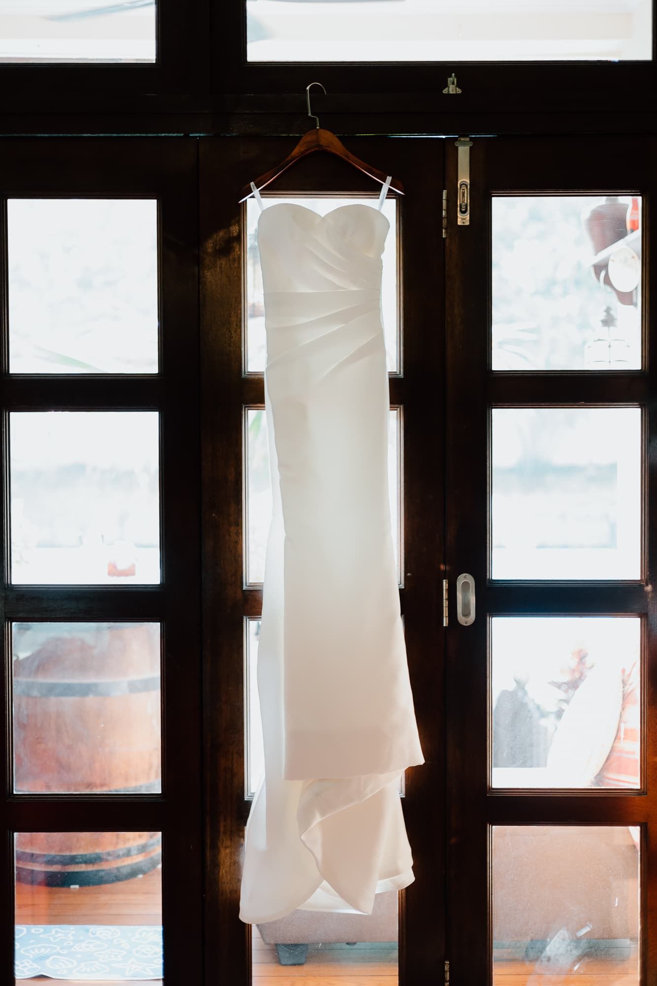 White wedding dress hanging elegantly against a backlit window with geometric panes.