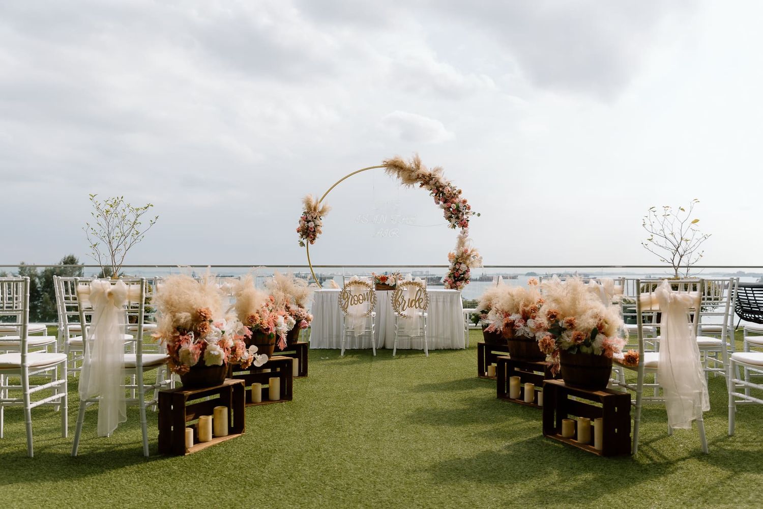 Outdoor wedding ceremony setup with wooden chairs and floral arrangements against ocean view.
