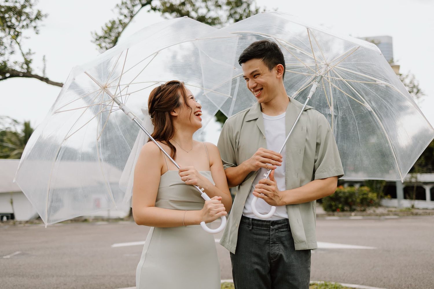Couple sharing laughs while holding clear umbrellas outdoors.