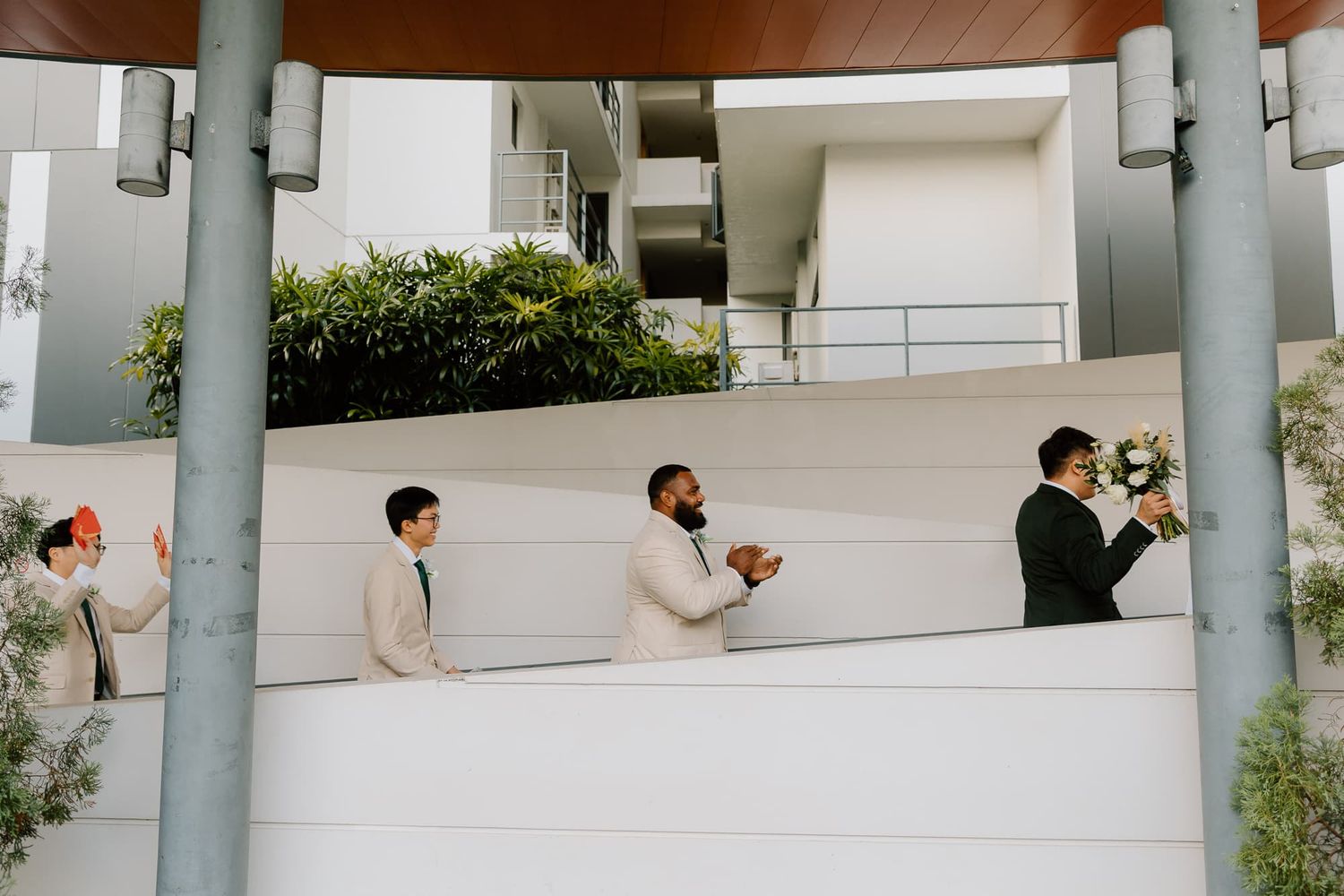 Wedding party members lined up along a modern architectural wall holding bouquets.