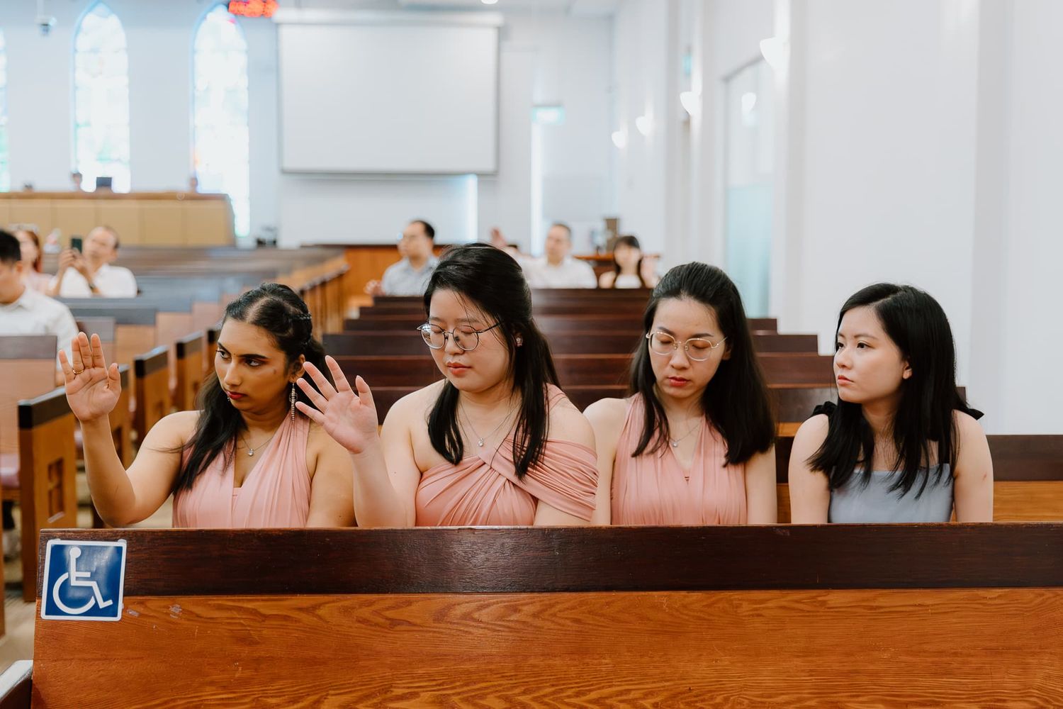 Bridesmaids in pink dresses seated together in a church pew during a wedding ceremony.