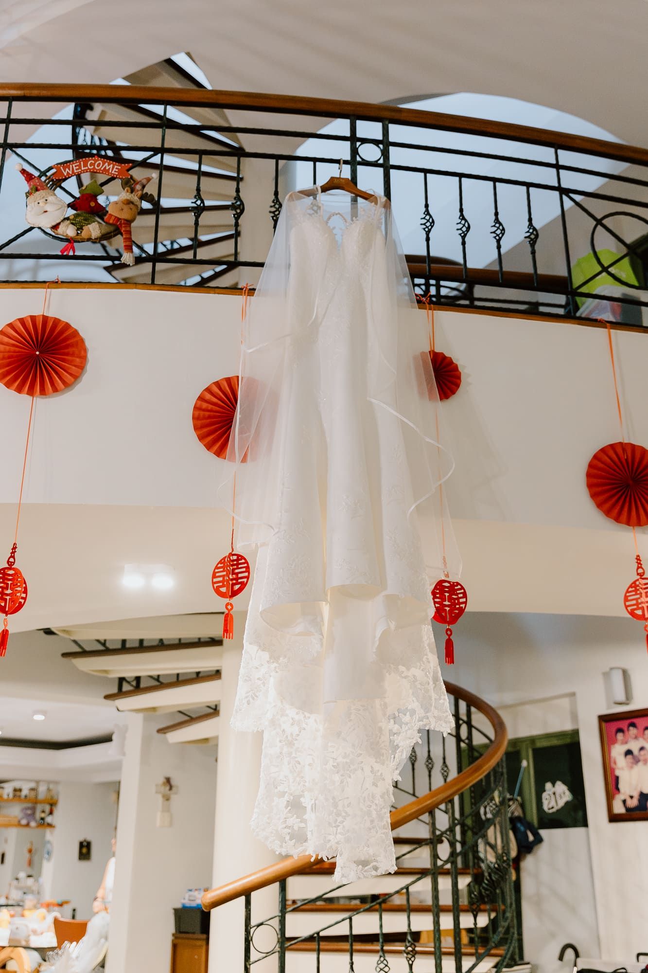 A white wedding dress hangs from a spiral staircase railing with red paper lanterns and fans decorating the space.