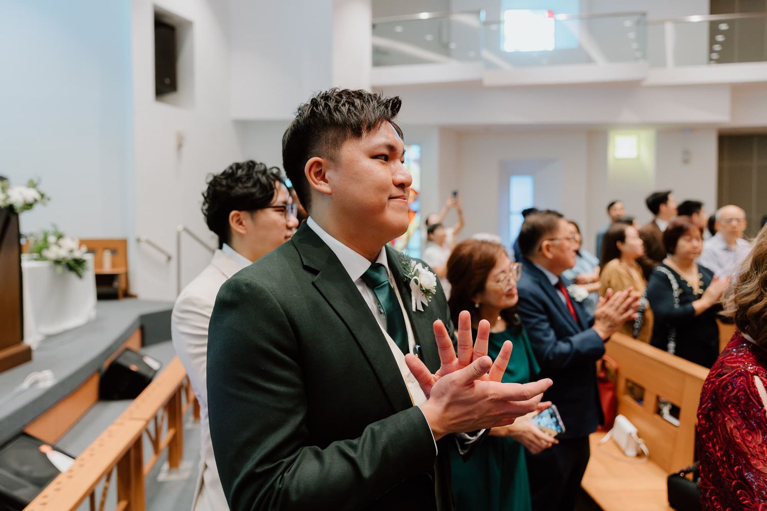 Wedding guests in formal attire applaud during joyful celebration in church.