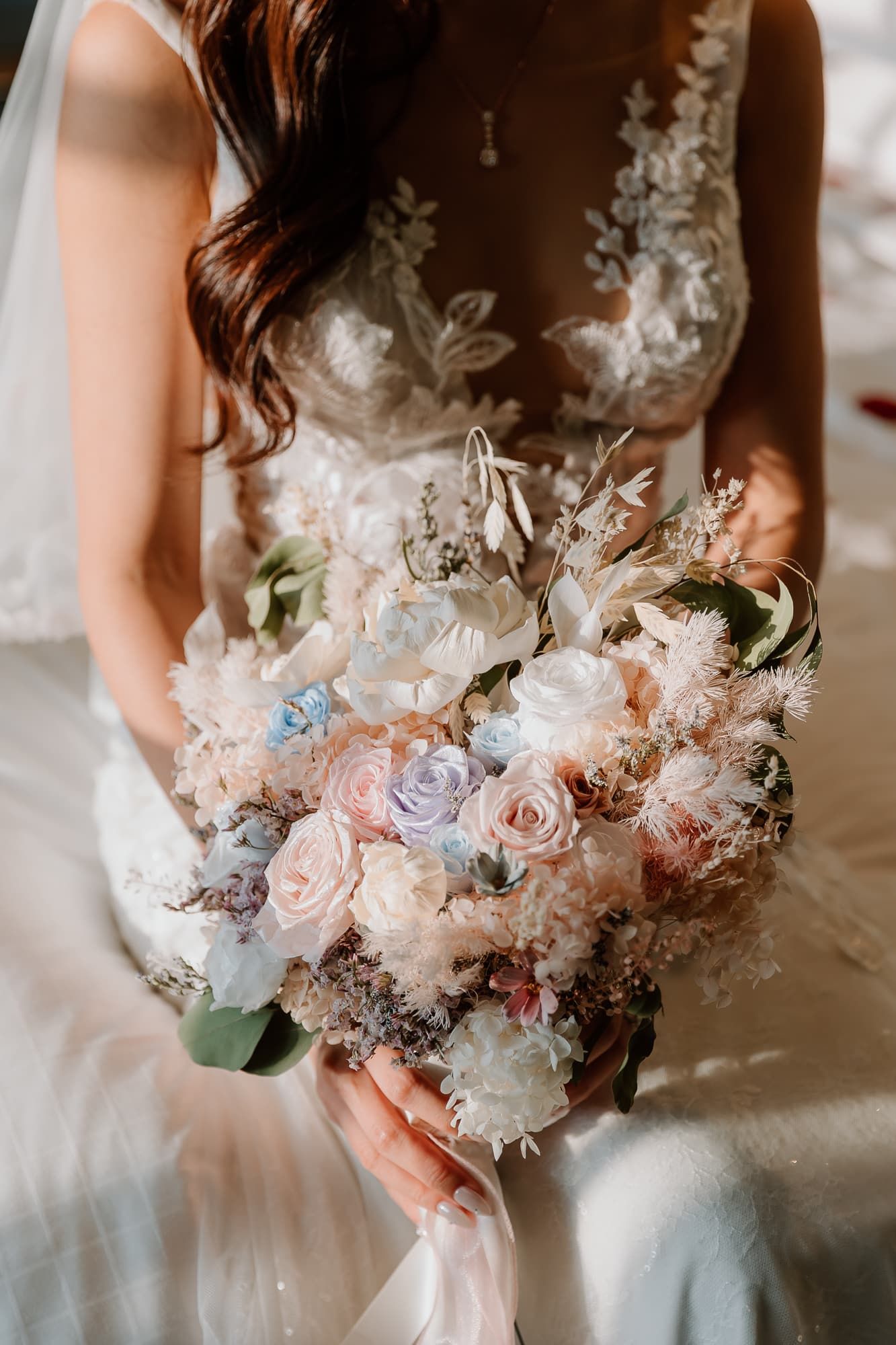 An elegant bridal bouquet featuring pink and blue roses with delicate dried flowers and greenery.