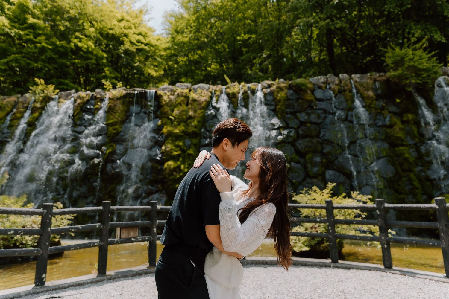 Couple sharing a romantic kiss in front of a lush waterfall backdrop at an outdoor wedding venue.
