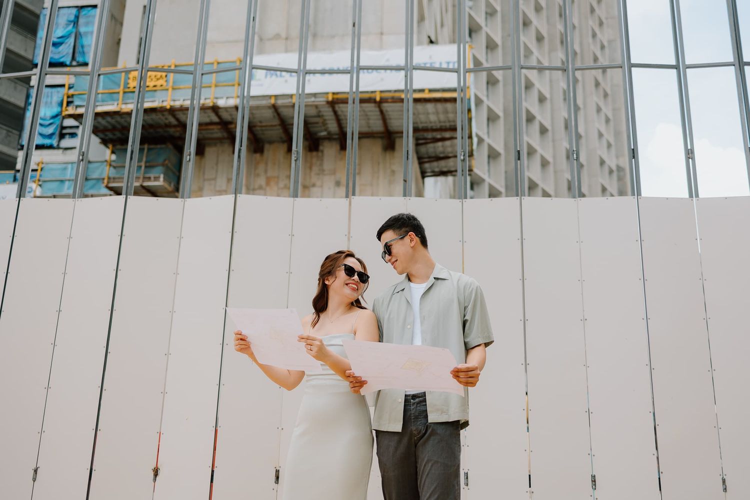 A couple laughing while looking at documents against a modern building exterior.