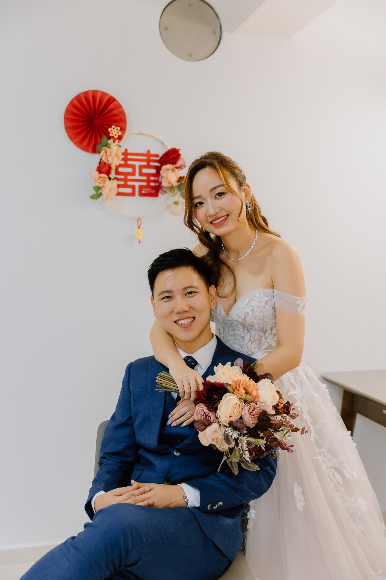 Couple in wedding attire sharing a romantic moment with traditional Chinese double happiness symbol and red fan.