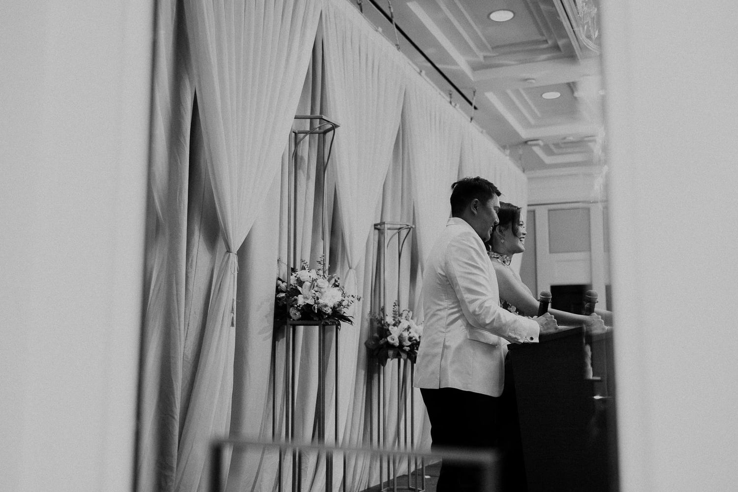 Piano player performs at an elegant event behind white curtains in black and white.