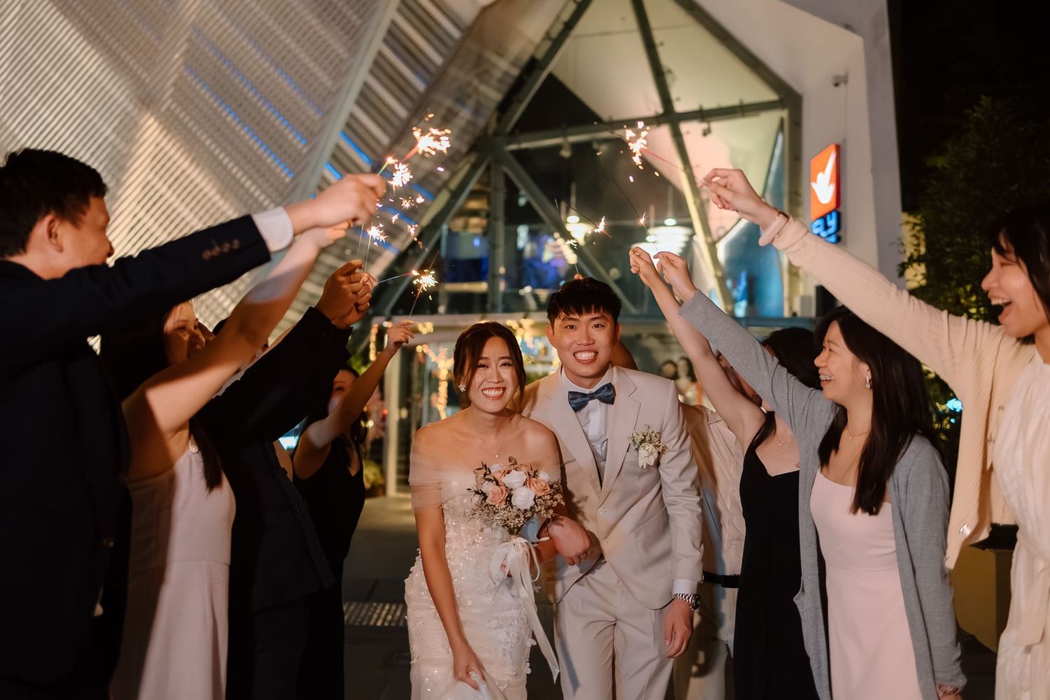 Wedding couple walks under sparklers held by guests in a modern venue.