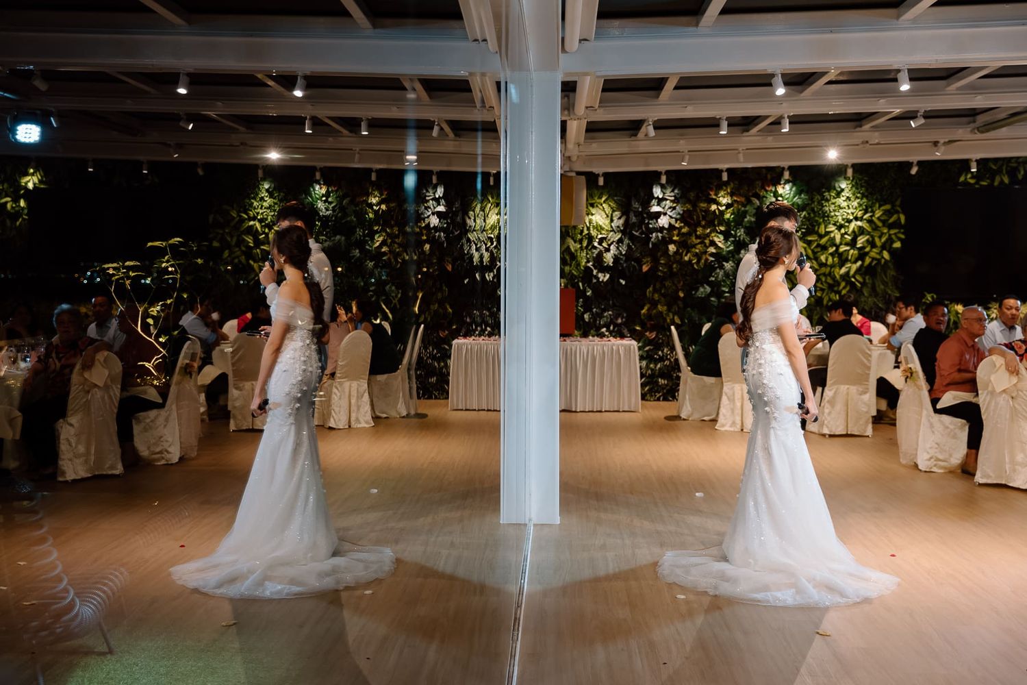 Bride in white dress reflected in mirror during wedding reception.