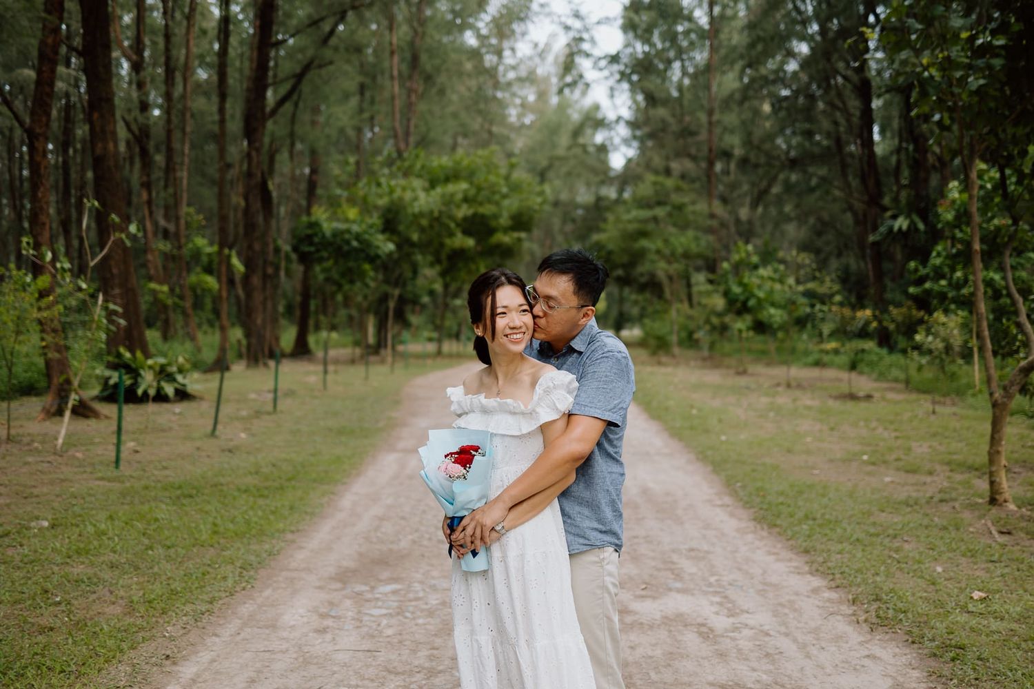 A couple shares a tender moment on a forest path with pine trees.