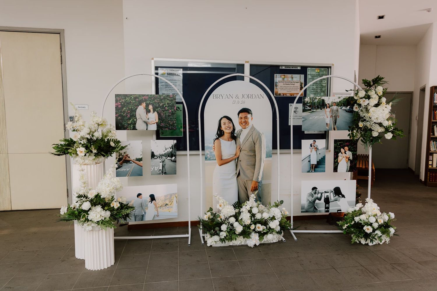 Modern wedding photo display with white floral arrangements and geometric frames on pedestals.