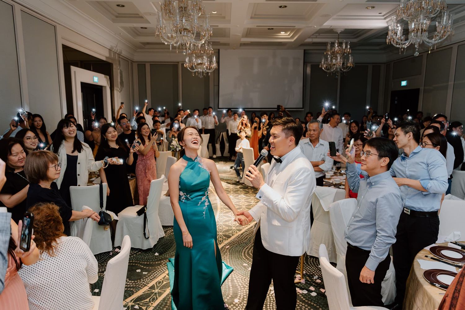 Wedding celebration in elegant ballroom with guests dancing and crystal chandeliers overhead.