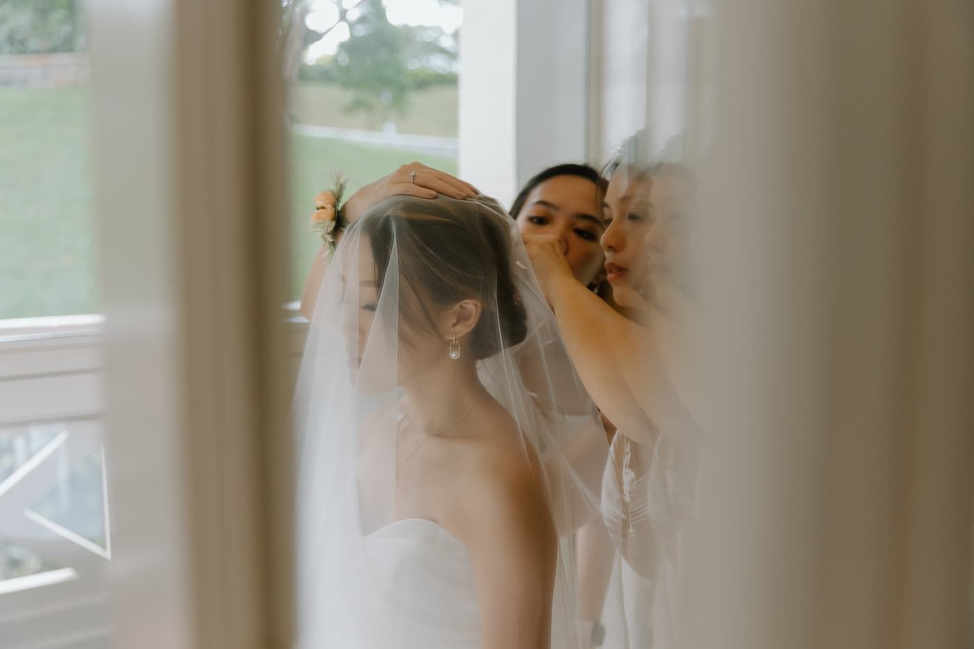 White bridal veil being adjusted in soft window light during wedding preparations.