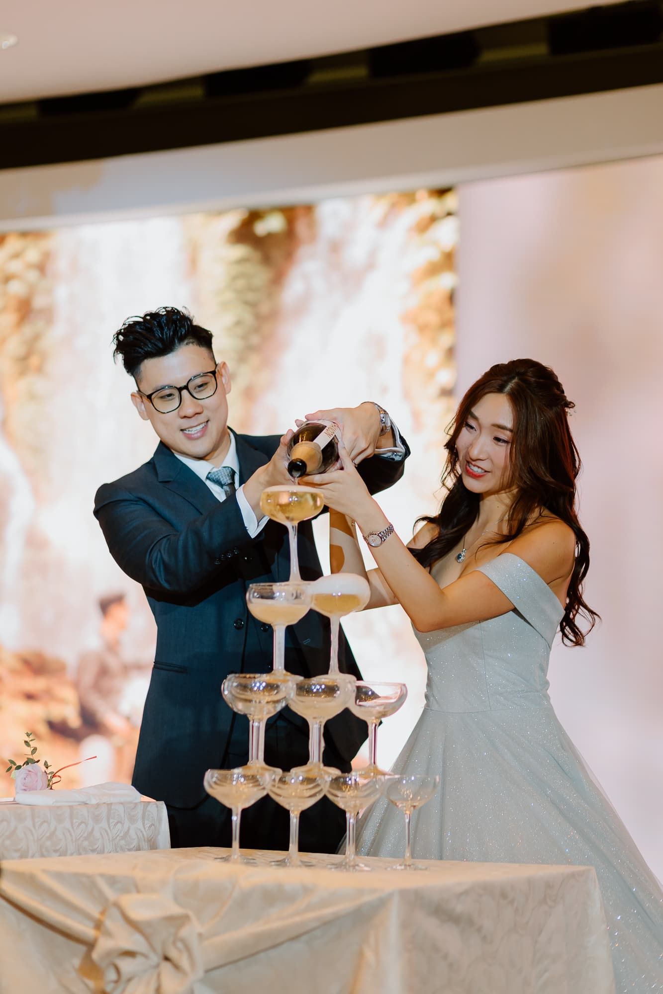 Wedding party stacking champagne glasses in a celebratory tower at the reception.