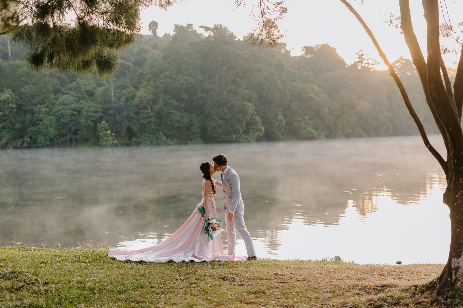 Misty lakeside wedding photography session during golden hour with trees in the background.