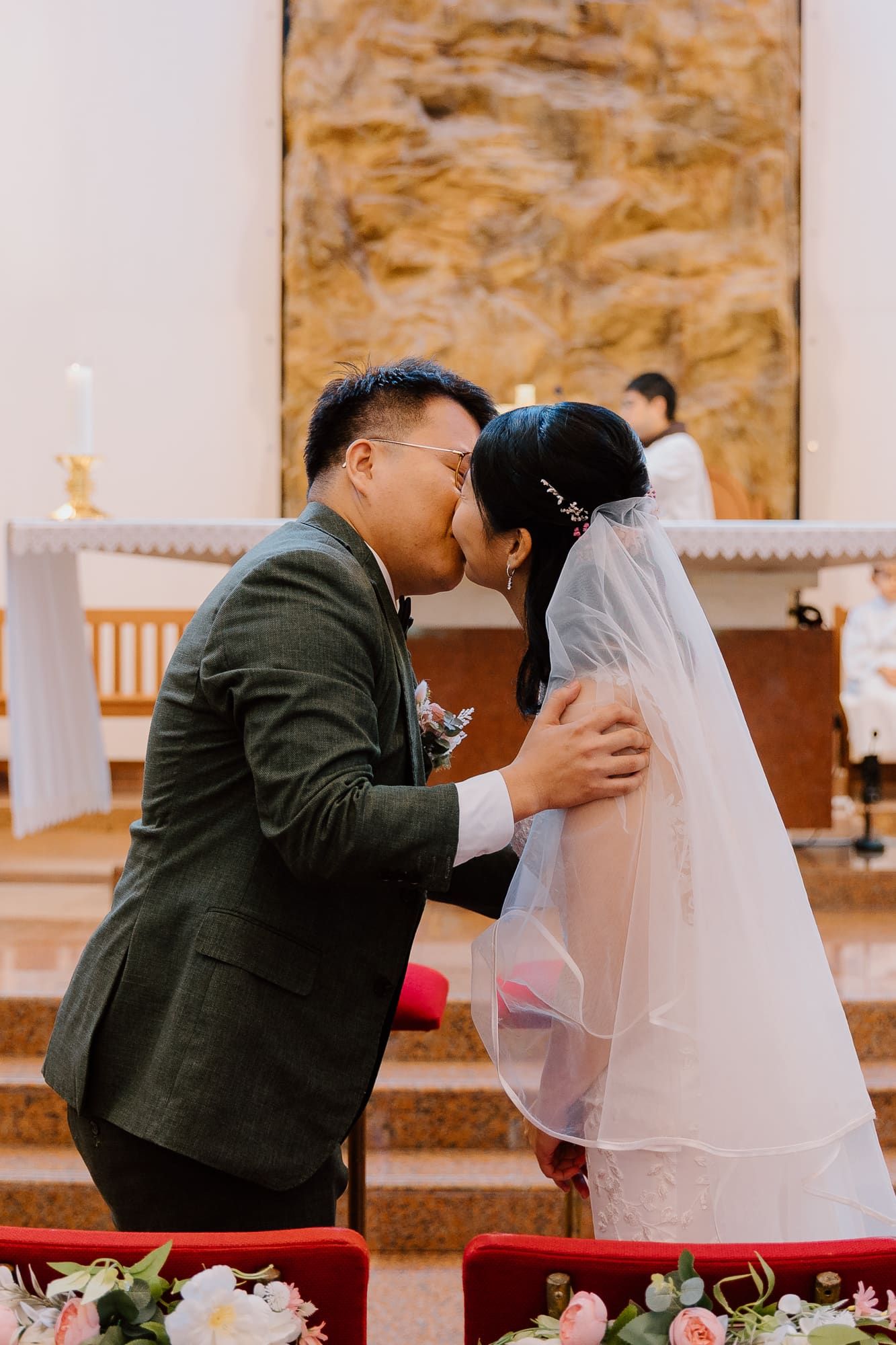 A tender moment during a wedding ceremony in a church with candles and floral decorations in view.