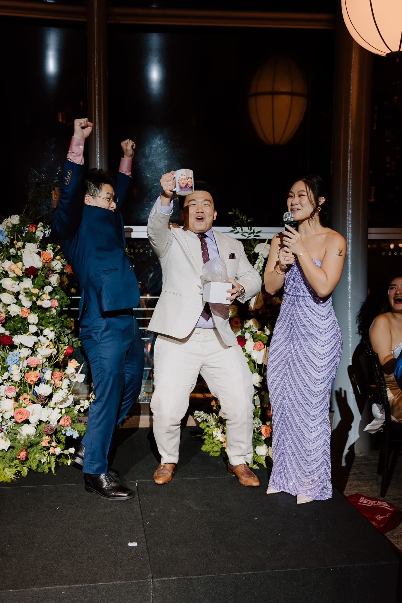 Wedding guests dance enthusiastically at reception with floral arrangements and lantern lighting.