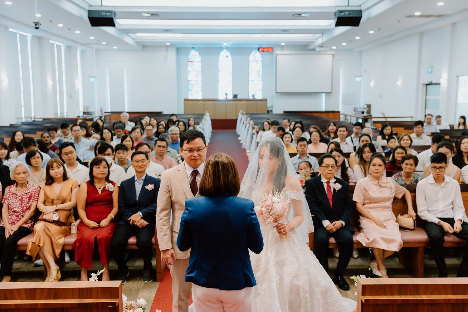 A crowded church wedding ceremony with guests filling the pews and natural light streaming through windows.