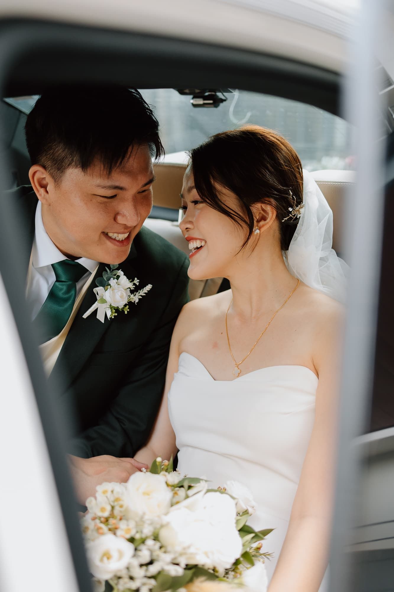 A tender moment between newlyweds sitting in a car, with white floral boutonniere and bridal bouquet visible.