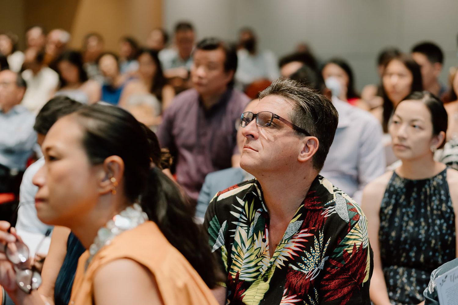 Wedding guests seated in rows watch the ceremony with attentive expressions.