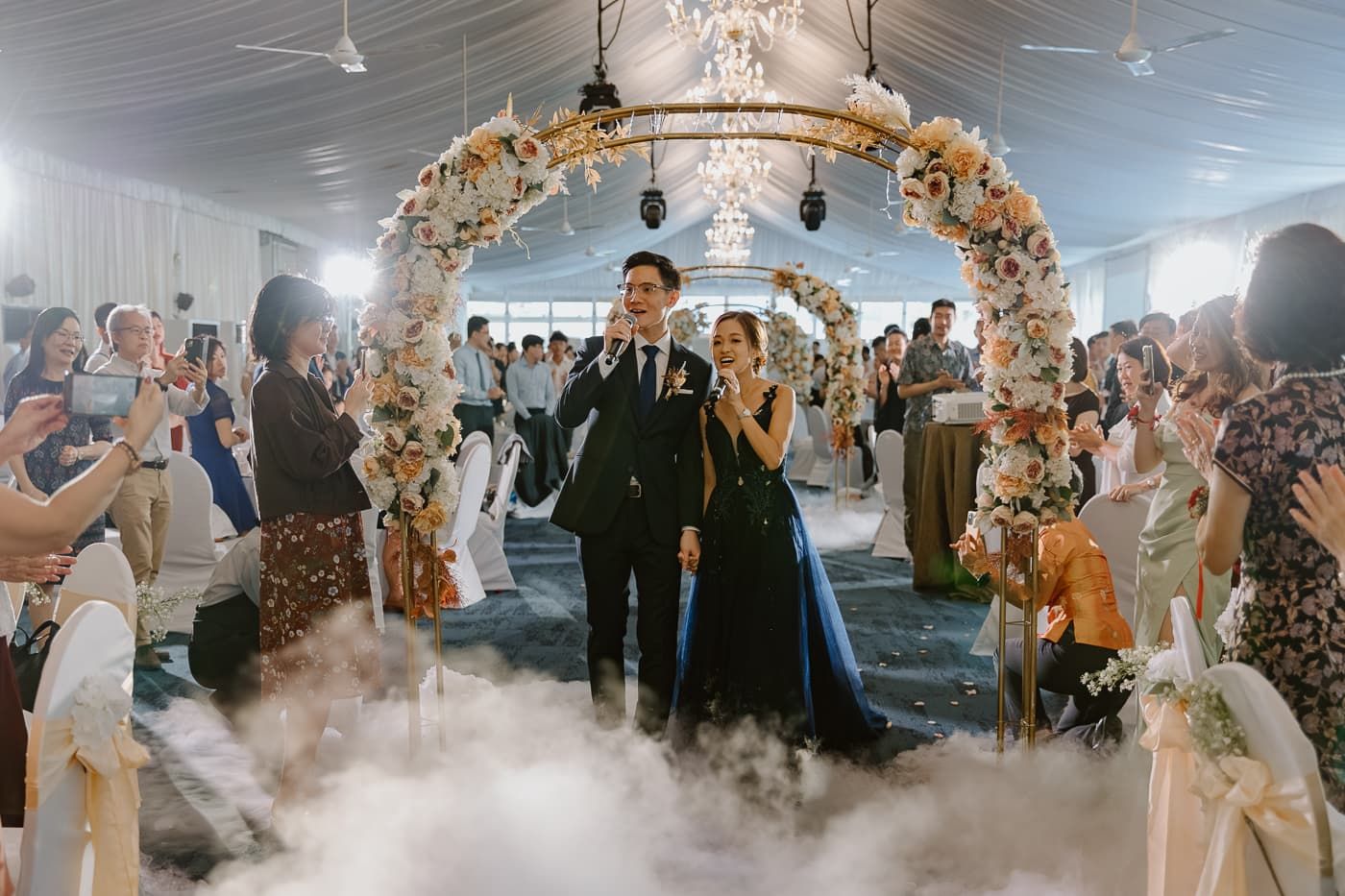 Dramatic wedding entrance with low-lying fog effects under a floral arch and chandelier.