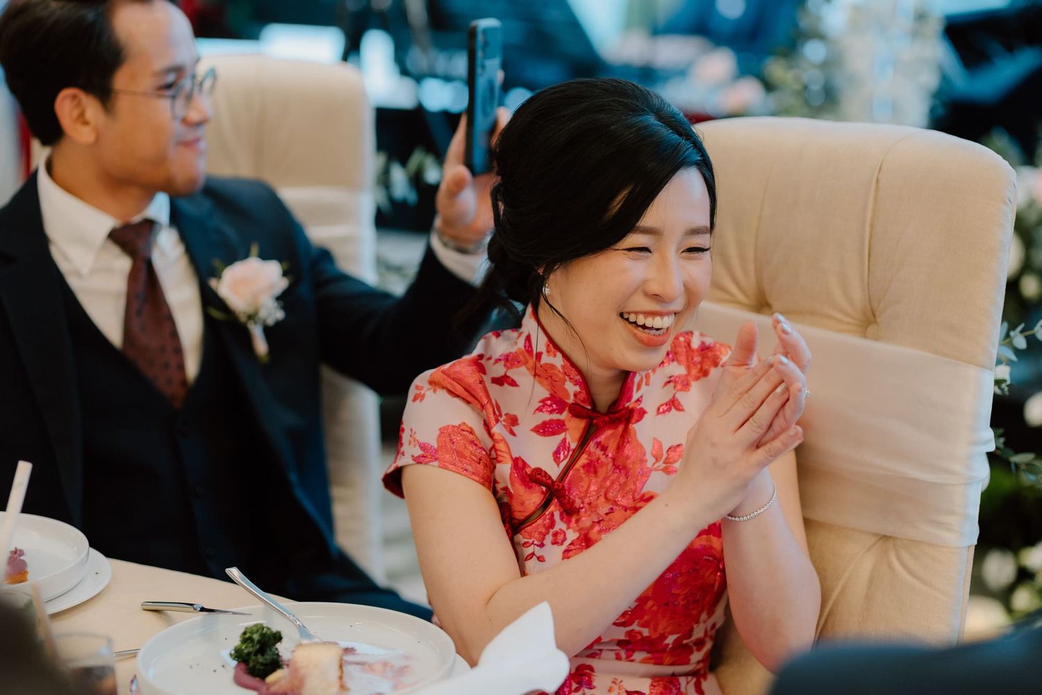 A person wearing a traditional red Chinese qipao dress laughs joyfully during a formal event.