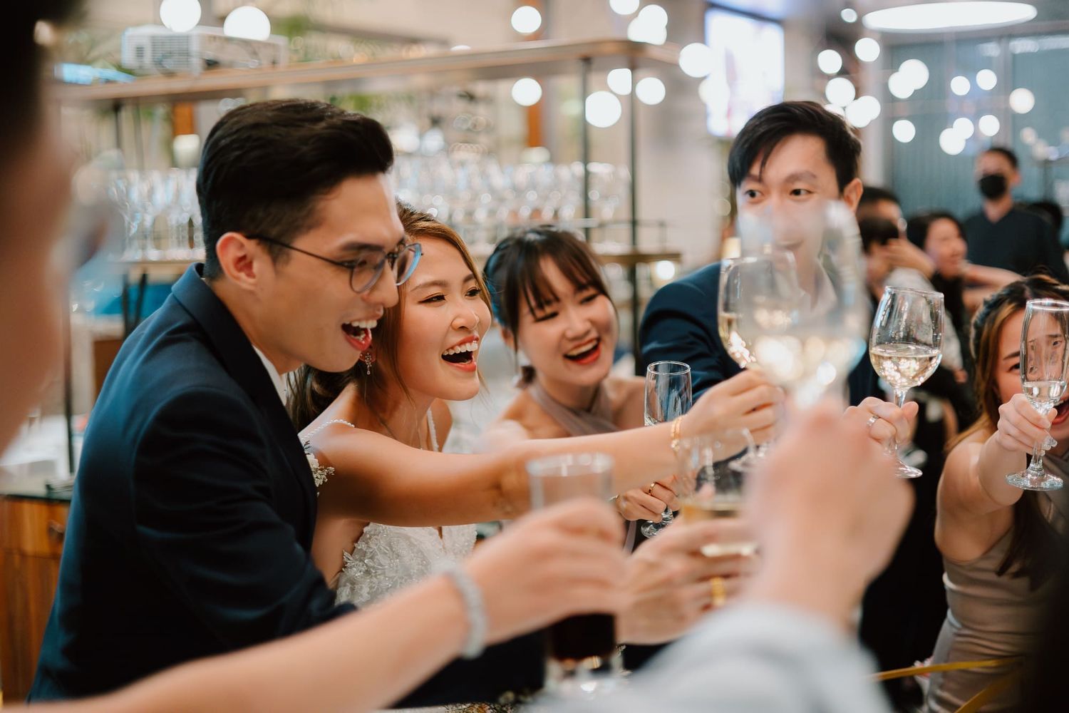 Happy party guests raise wine glasses in a toast at a celebratory dinner gathering with twinkling lights behind them.
