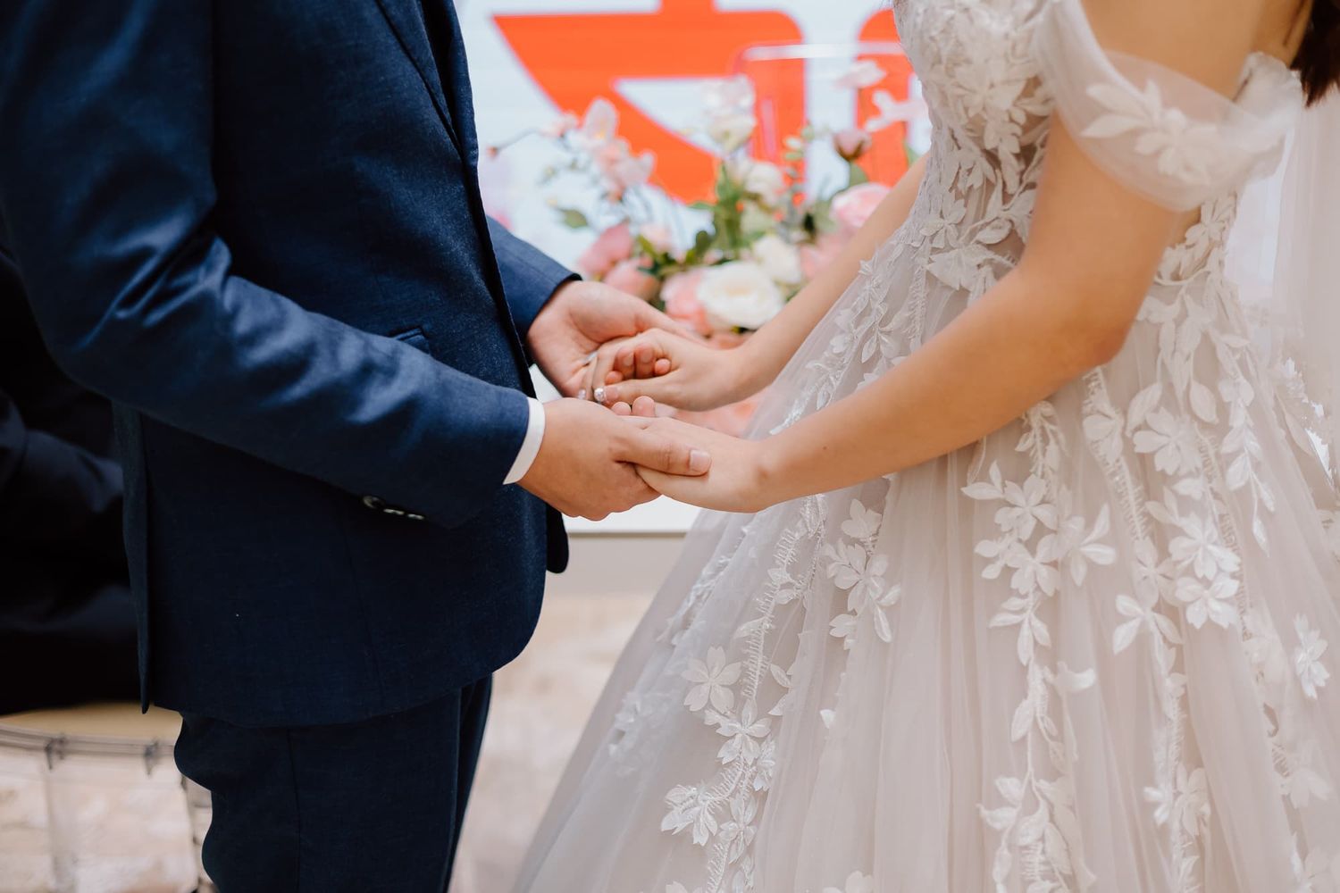 Close-up of bride in lace dress and groom in navy suit during wedding ceremony.